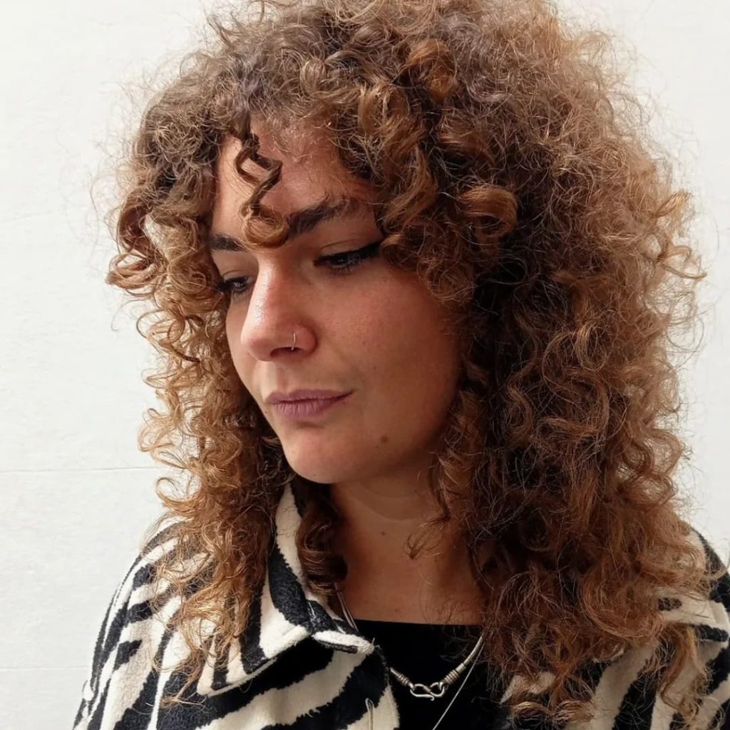30 Best Curly Wolf Cut Ideas to Showcase Your Beautiful Curls 26 Light Brown Curly Wolf Cut with Wispy Bangs