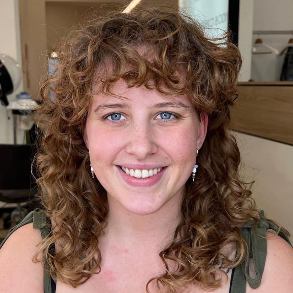 30 Best Curly Wolf Cut Ideas to Showcase Your Beautiful Curls 9 Light Brown Curly Wolf Cut with Bangs